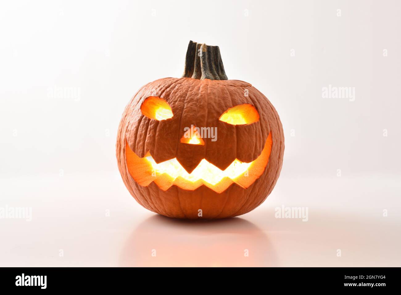 Citrouilles d'halloween sculptées et illuminées préparées pour les fêtes reflétées sur une table blanche et un fond blanc isolé. Vue avant. Comp. Horizontale Banque D'Images
