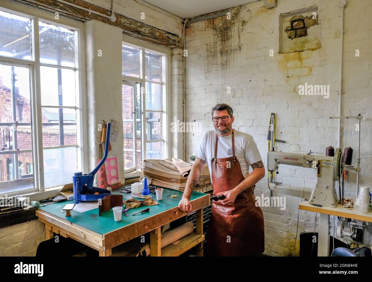 Vue intérieure de Portland Works, Sheffield, une ancienne coutellerie est désormais transformée en espaces d'artisanat. Un ouvrier du cuir est debout par des machines industrielles. Banque D'Images