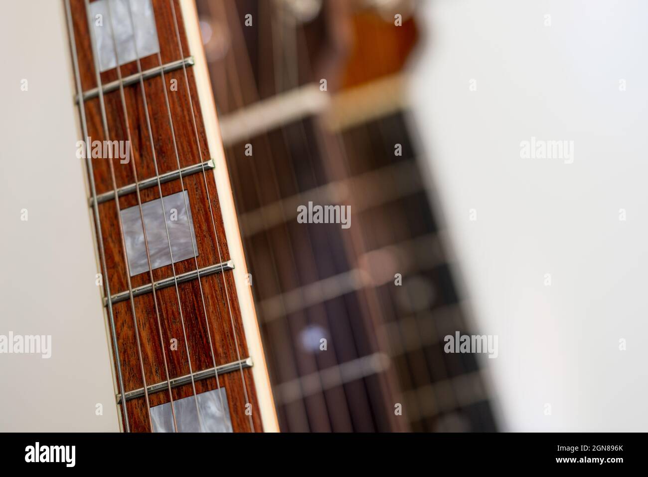 Gros plan d'un tableau incrusté de perles de bois de rose avec six cordes sur une guitare électrique avec des guitares hors du focus en arrière-plan Banque D'Images