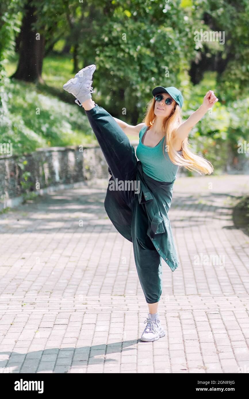 Une fille en vêtements de hip-hop émeraude fait une balançoire de jambe dans la ruelle du parc Banque D'Images