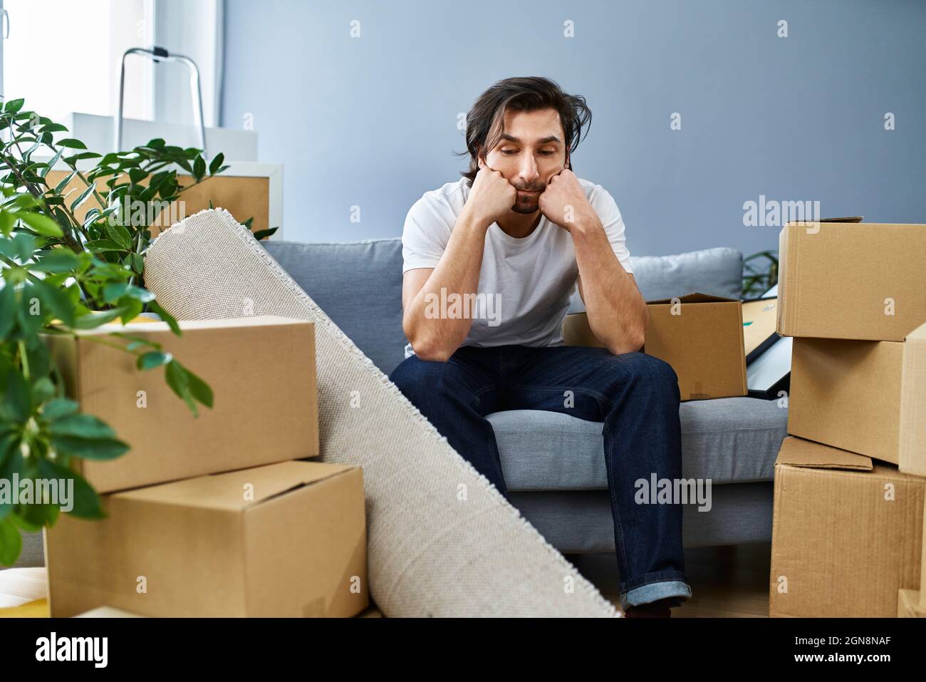 Homme contrarié assis sur un canapé au milieu de boîtes en carton à la maison Banque D'Images