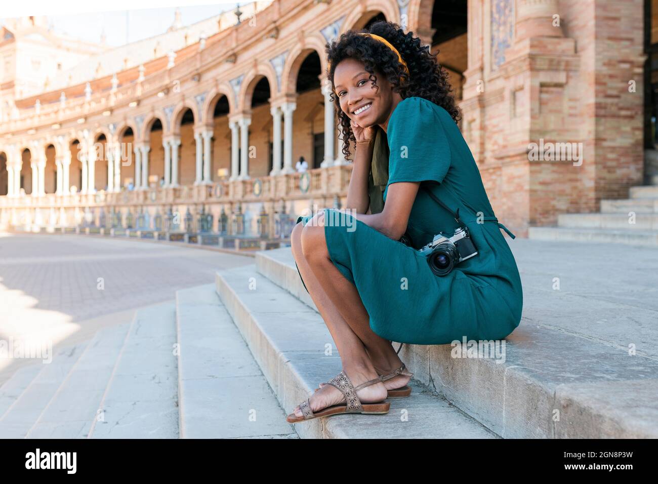 Jeune femme souriante avec caméra assise sur les marches de la Plaza de Espana, Séville, Espagne Banque D'Images