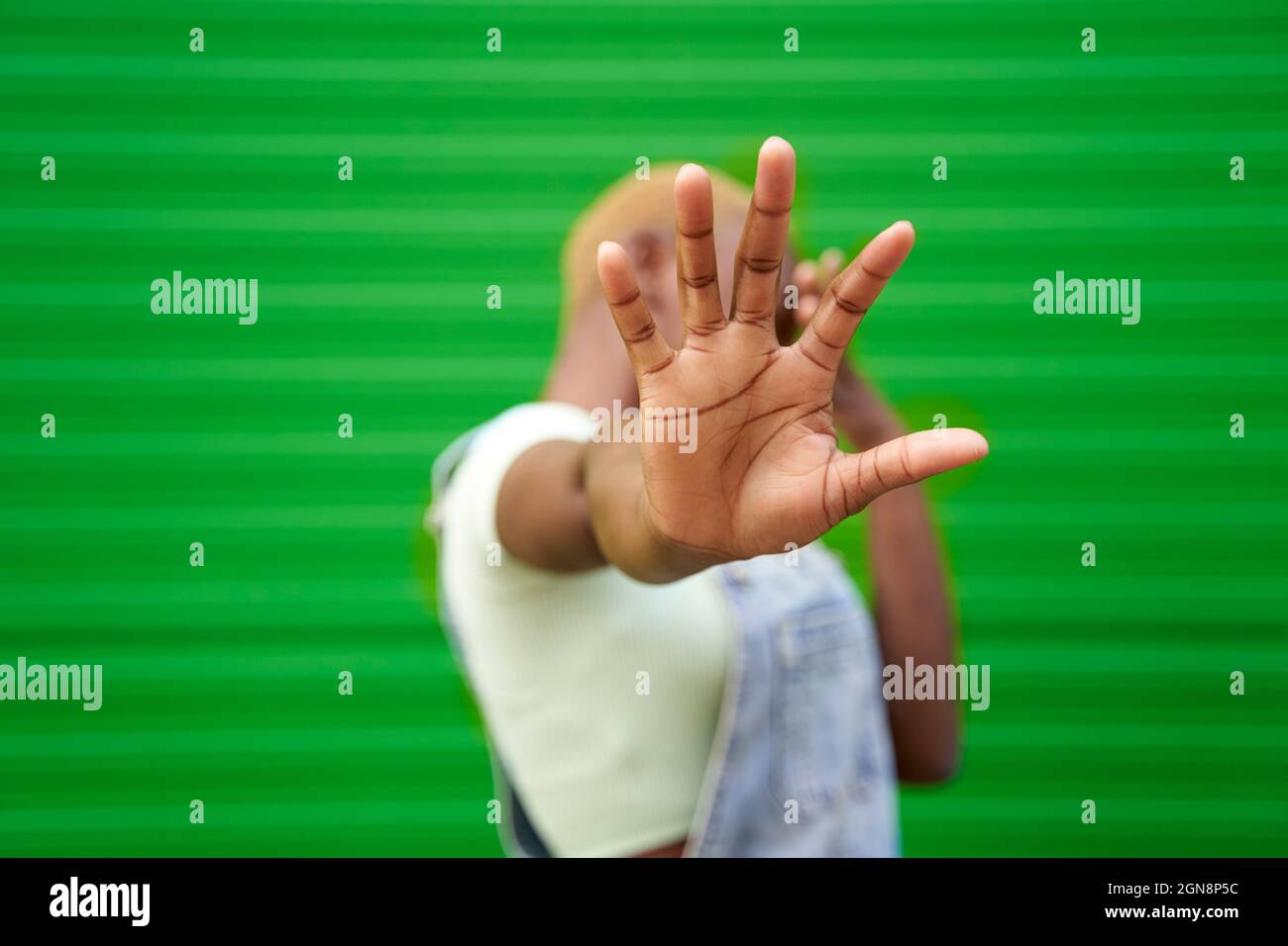 Jeune femme signe d'arrêt de gestuelle devant le mur vert Banque D'Images