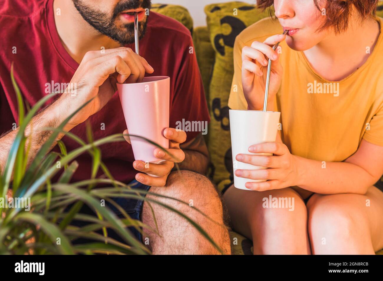 Couple tenant des verres de bambou tout en buvant de paille de métal à la maison Banque D'Images
