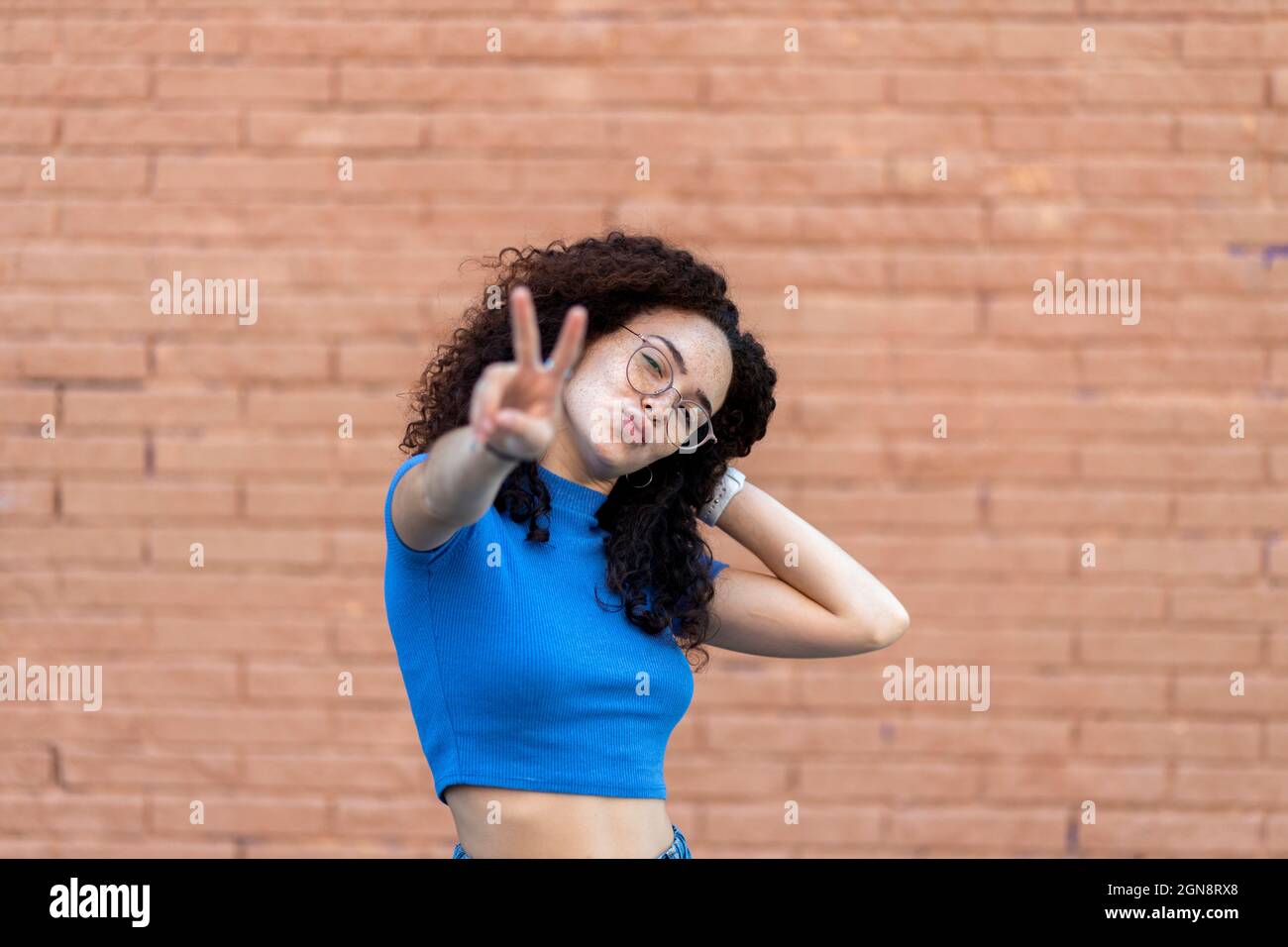 Femme avec main dans les cheveux montrant le geste de paix devant le mur Banque D'Images