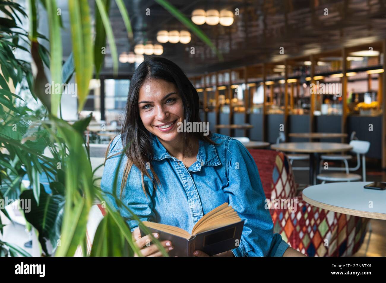 Femme indépendante avec livre assis au café Banque D'Images