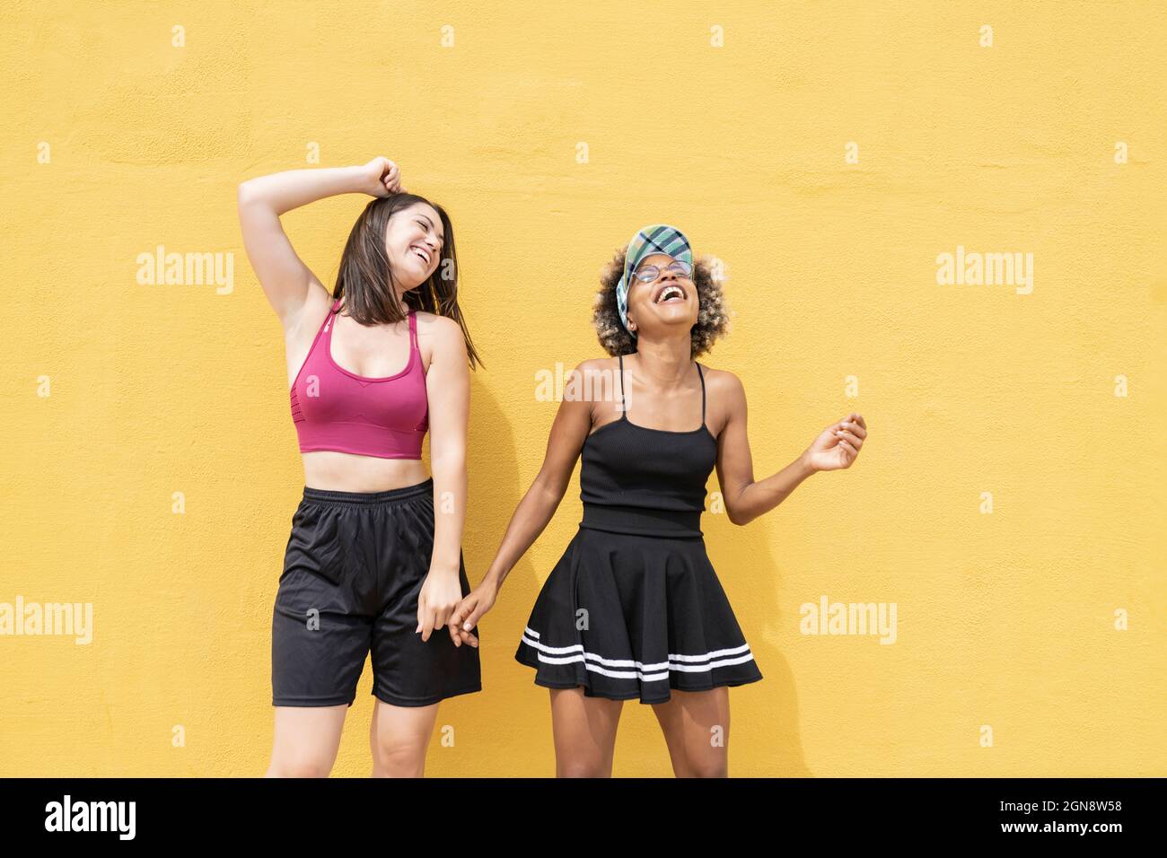 Des amis multiethniques joyeux dansant devant le mur jaune Banque D'Images