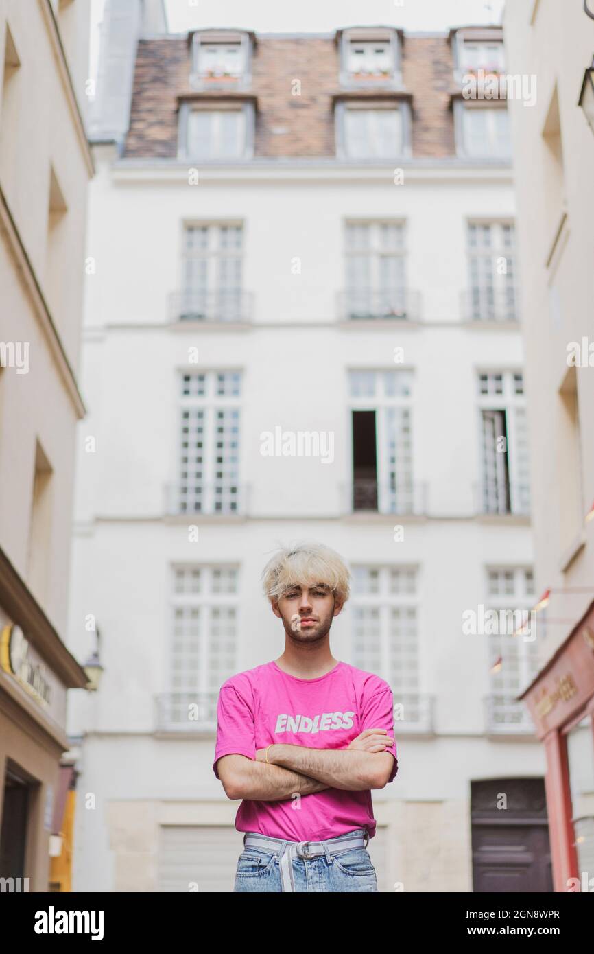 Jeune homme gay debout avec les armes croisées devant le bâtiment Banque D'Images