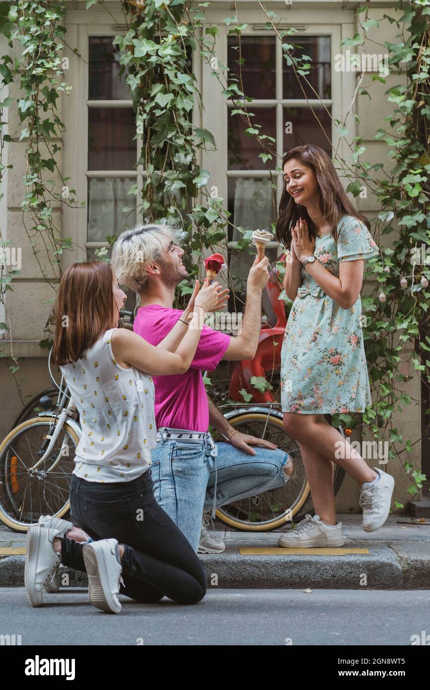 La jeune femme et l'homme s'agenouillent tout en tenant de la crème glacée pour une amie sur le sentier Banque D'Images