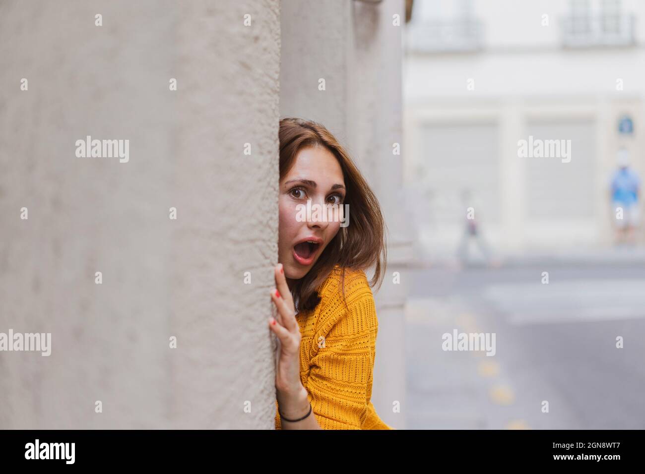 Femme surprise avec les cheveux bruns peeking du mur Banque D'Images