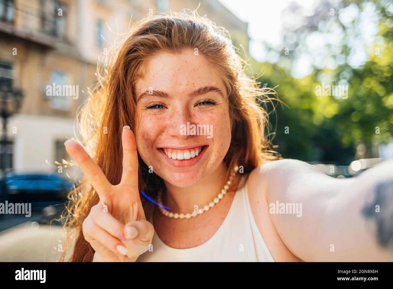 Femme souriante à tête rouge montrant le geste de paix tout en prenant le selfie Banque D'Images