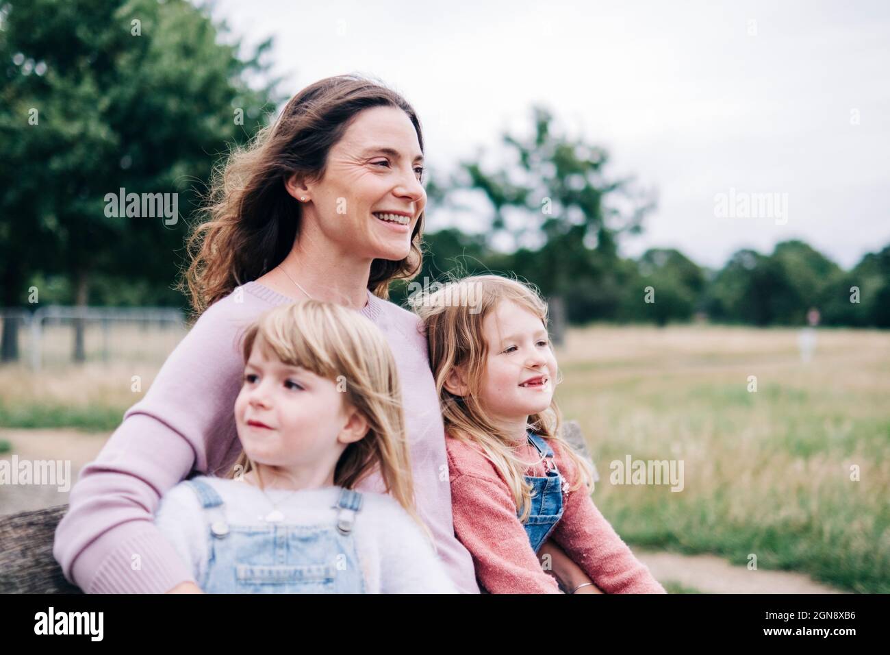 Mère souriante assise avec des filles dans le parc public Banque D'Images