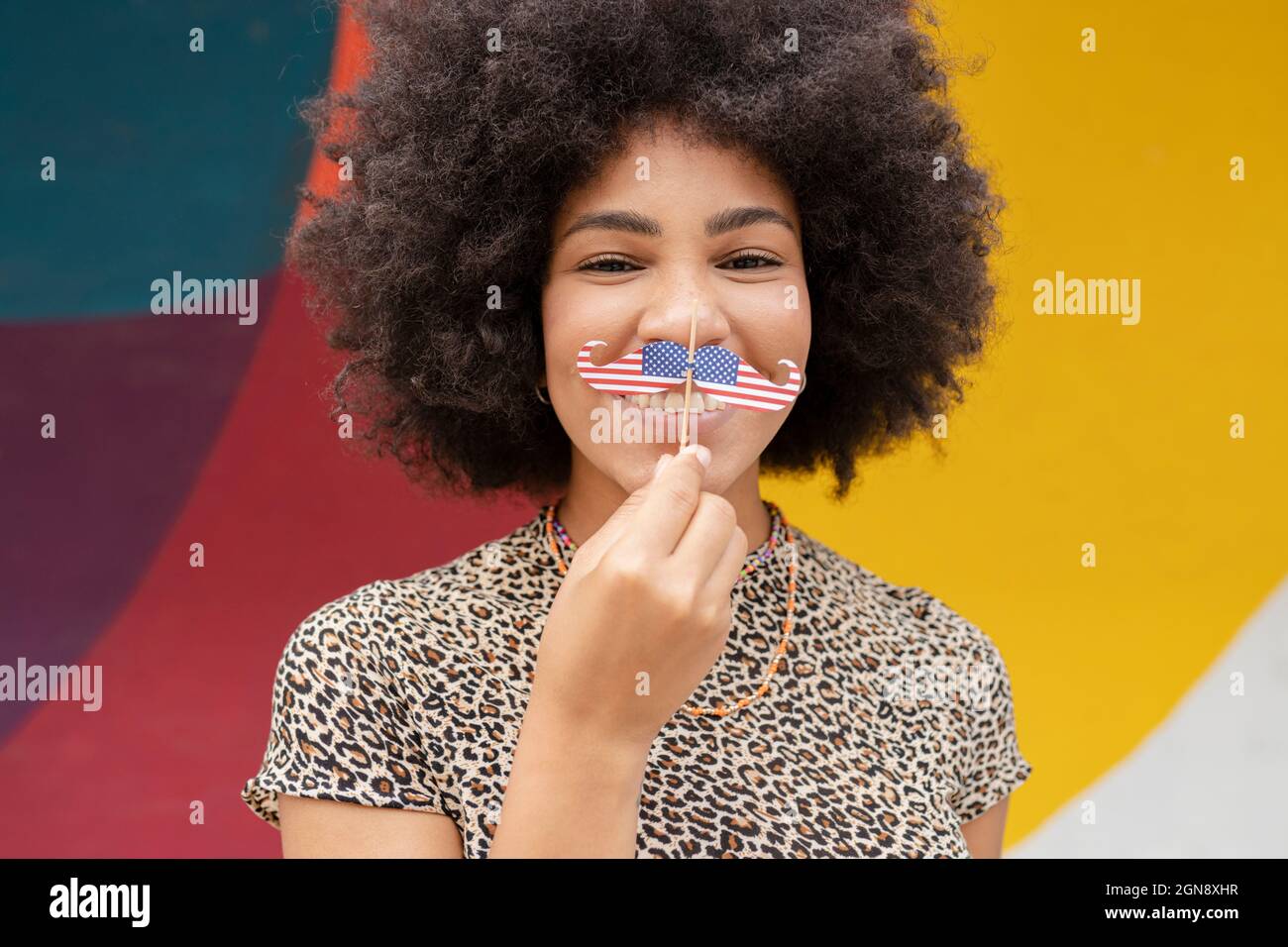 Femme afro tenant le support de moustache devant le mur Banque D'Images