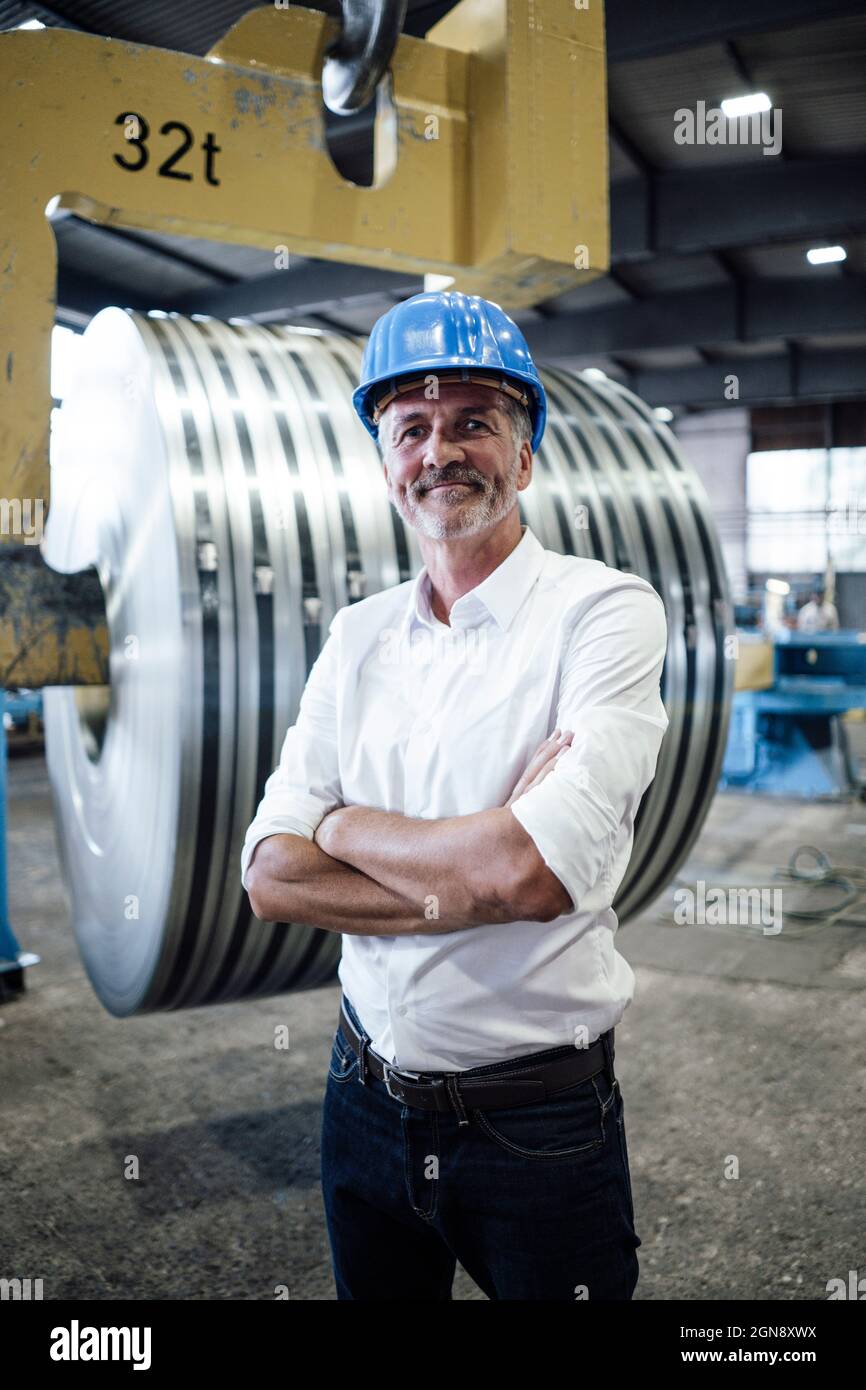 Professionnel souriant avec bras croisés debout dans une aciérie Banque D'Images