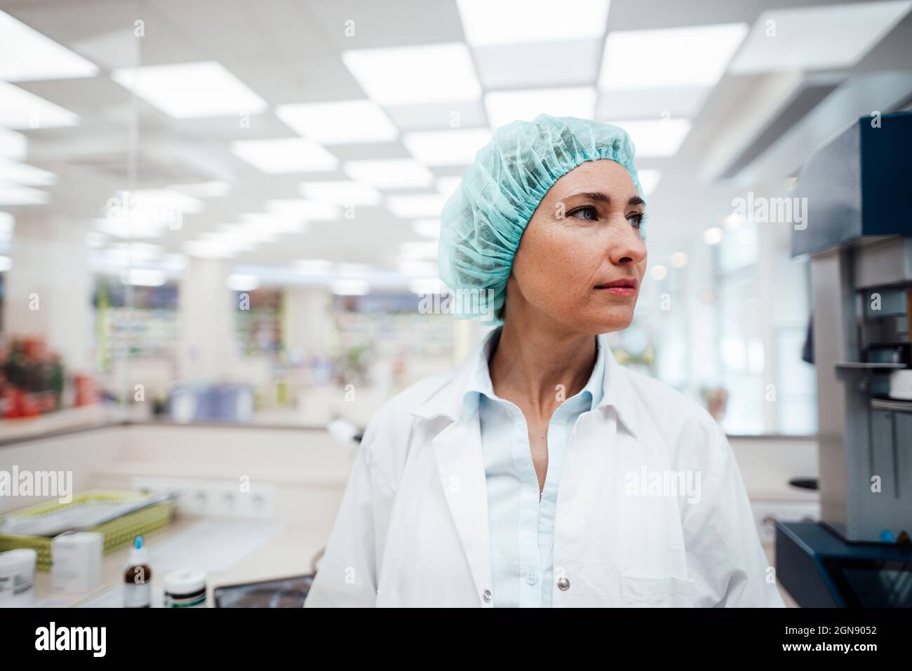 Une pharmacienne portant un capuchon chirurgical en regardant à l'extérieur pendant qu'elle se tient au laboratoire Banque D'Images