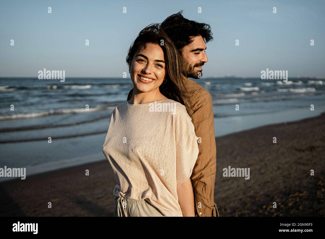 Homme et femme souriants se tenant dos à dos à la plage Banque D'Images