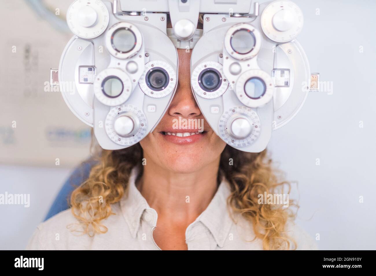 Patiente souriante examinant la vue par le biais d'un phoropter dans une clinique médicale Banque D'Images
