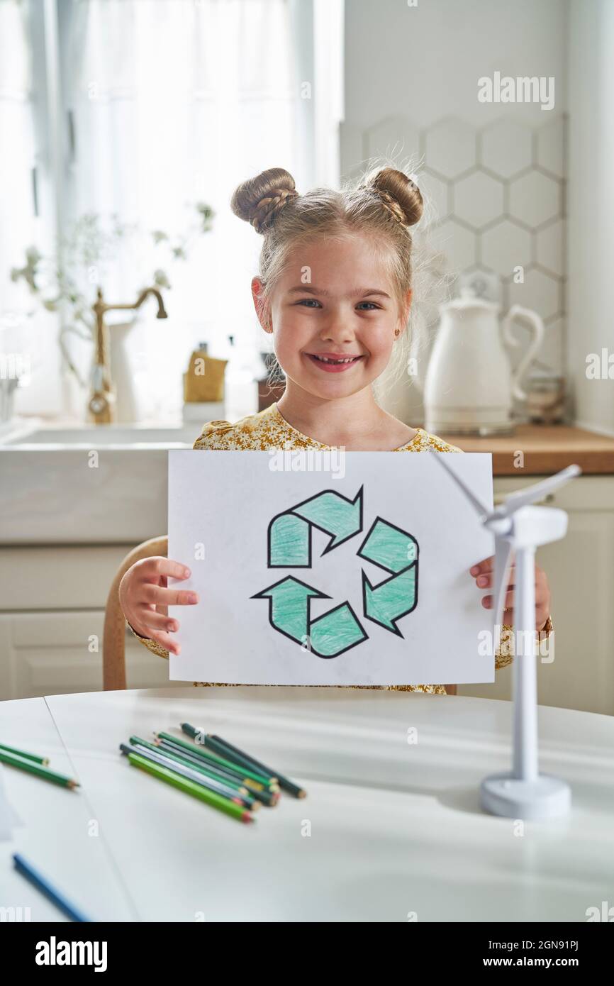 Fille souriante tenant le symbole de recyclage dessin sur papier à table Banque D'Images
