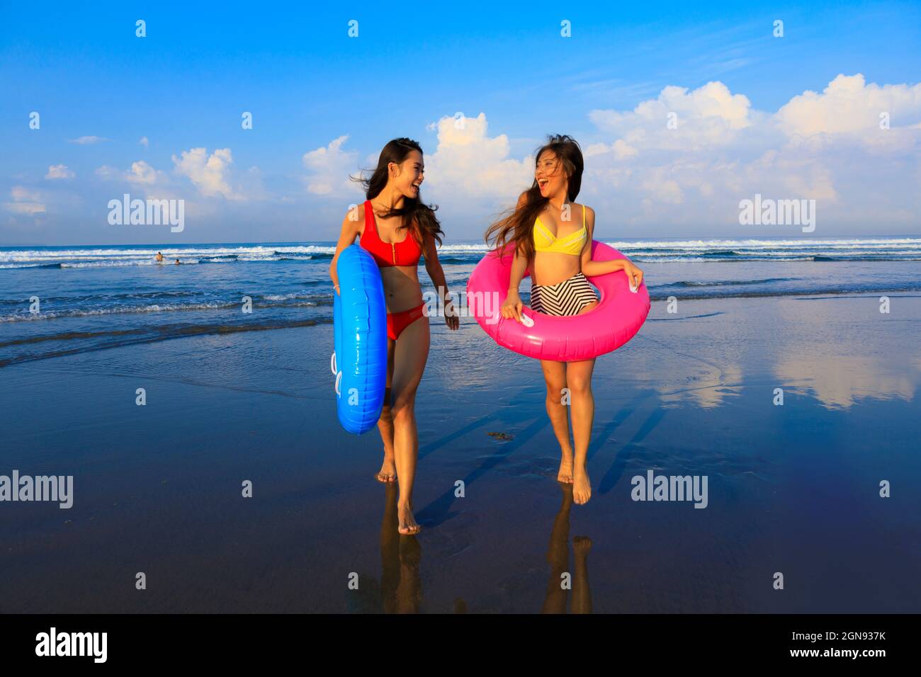 Des amies gaies avec des anneaux gonflables qui s'amusent à la plage Banque D'Images