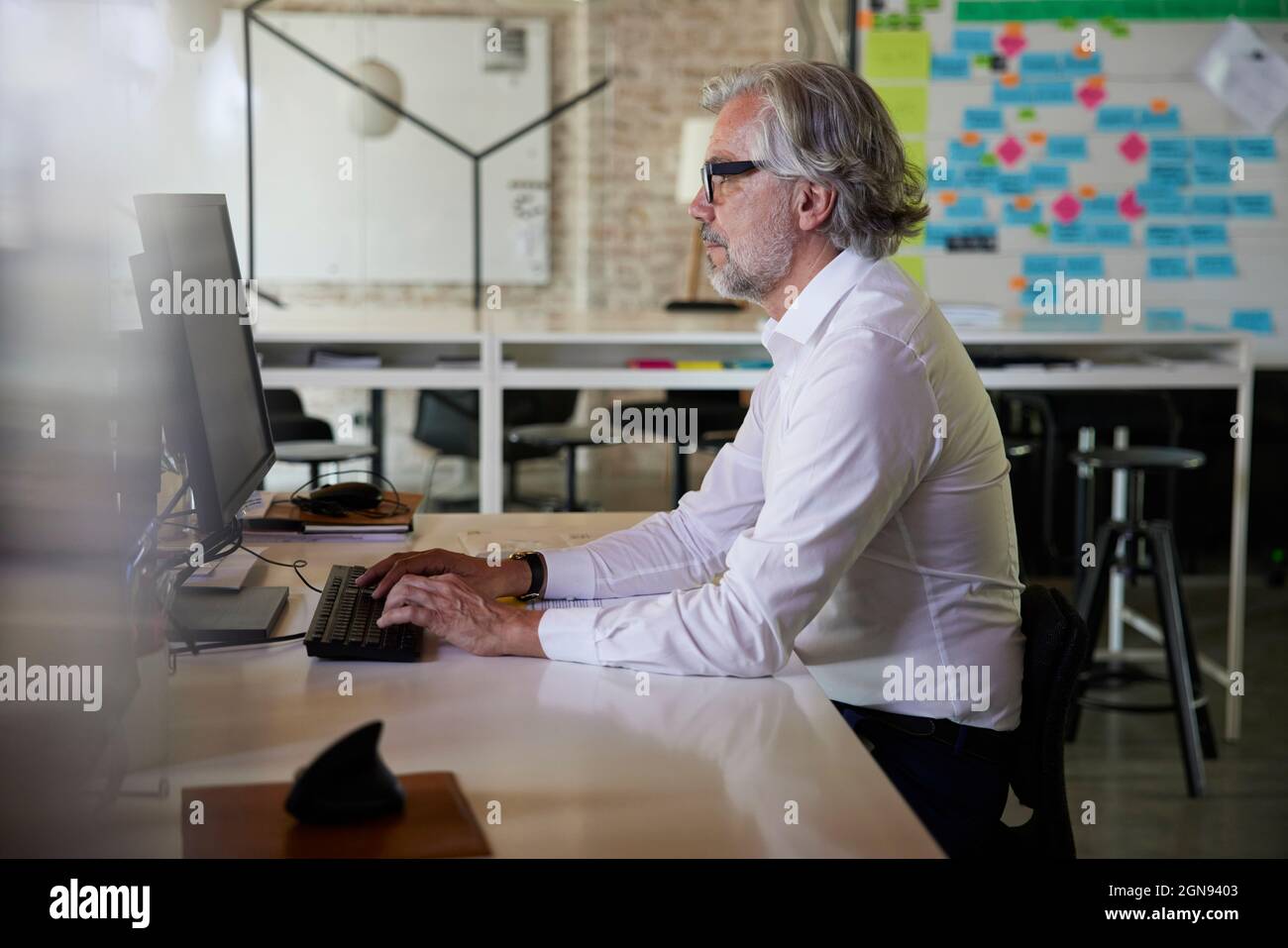 Homme d'affaires mature travaillant sur un ordinateur tout en étant assis au bureau Banque D'Images