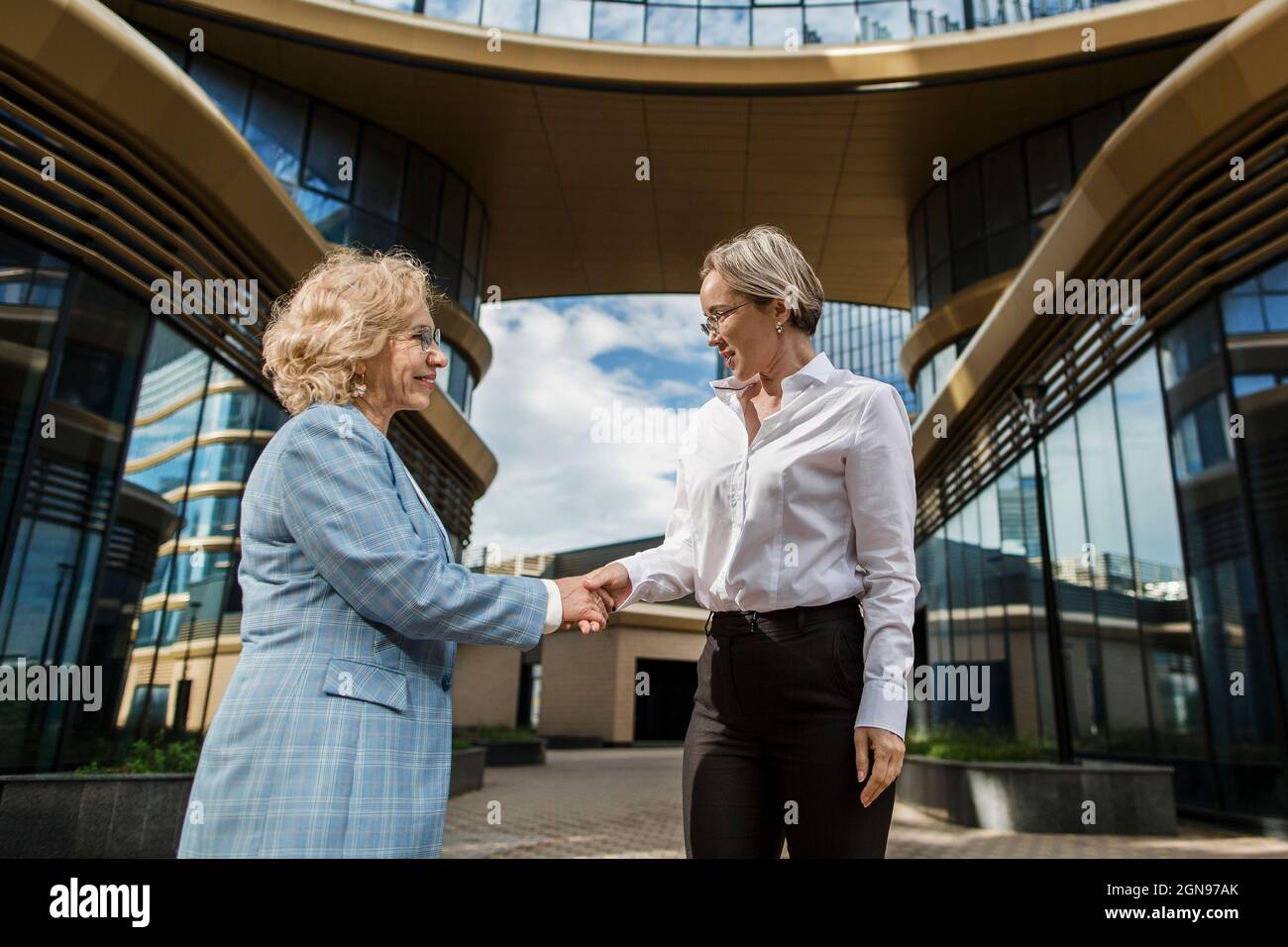 Femmes d'affaires se serrant la main en se tenant devant le bâtiment Banque D'Images