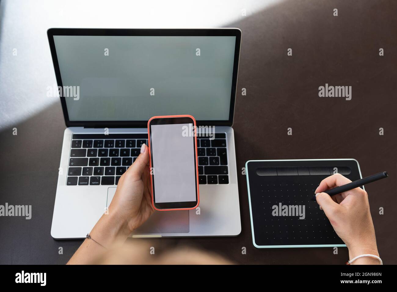 Femme graphiste utilisant un téléphone portable et une tablette graphique sur une table de café Banque D'Images