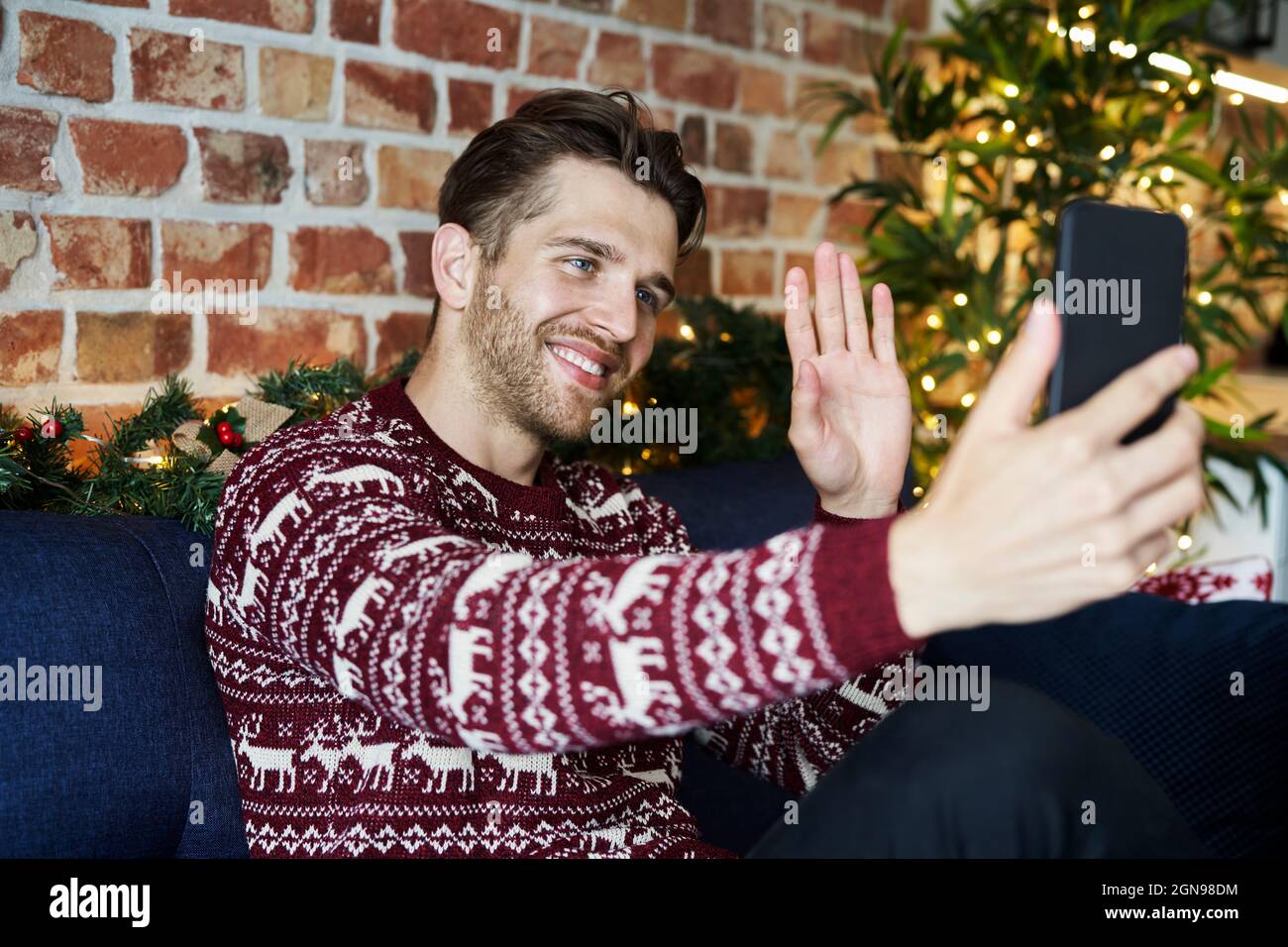 Un homme souriant se fait passer la main pour passer un appel vidéo depuis un téléphone portable à la maison Banque D'Images