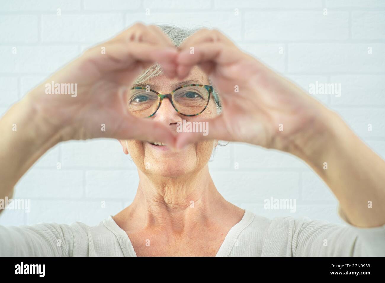 Femme âgée souriante qui fait le cœur avec les mains devant le mur Banque D'Images