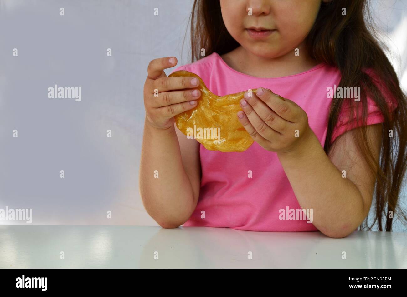 Mignon drôle de jouer fille avec slime coloré isolé sur fond blanc. Petite fille étirant jaune citron vert sur les côtés. Les enfants jouent à la chaux Banque D'Images