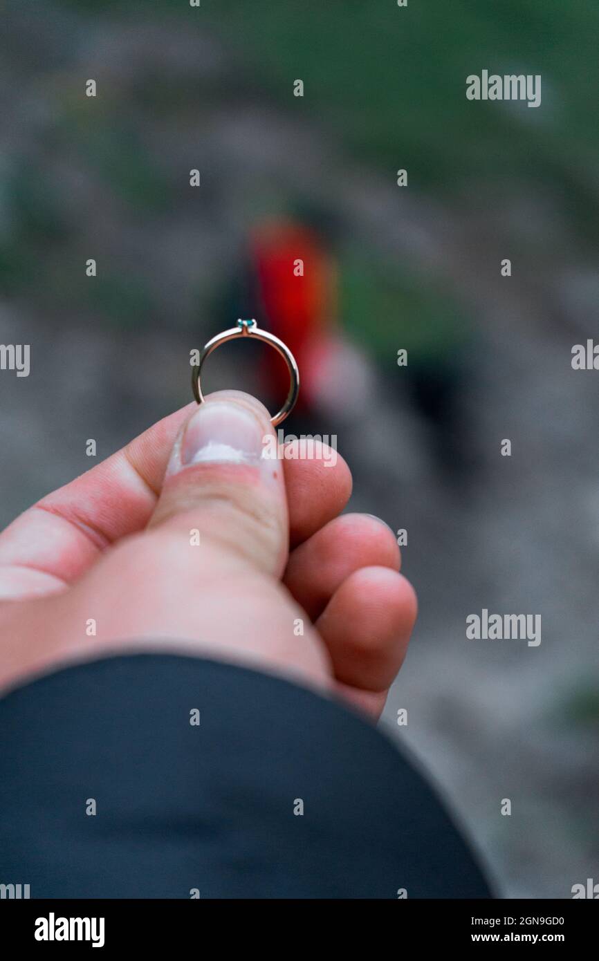 Main masculine tenant un anneau sur un fond flou d'une femme - proposition de mariage Banque D'Images