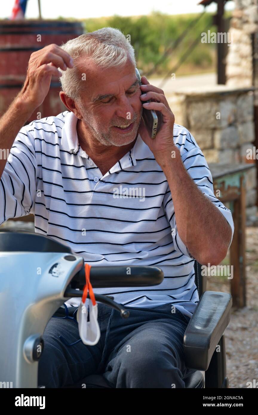 Homme senior assis dans un fauteuil roulant électrique et utilisant un téléphone portable Banque D'Images
