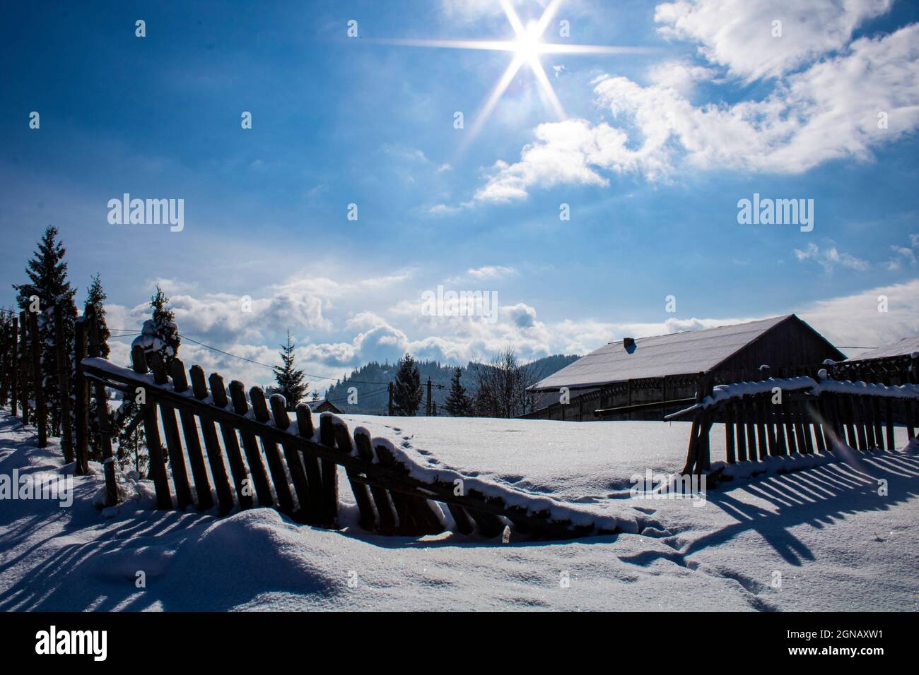 Paysage hivernal merveilleux, une journée ensoleillée remplie de neige. Une maison sur la colline et une clôture cassée. Banque D'Images