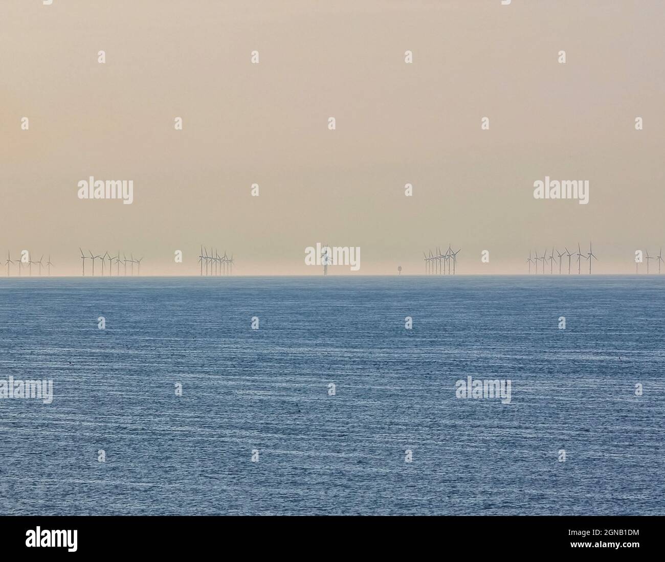 Les moulins à vent d'un parc d'éoliennes offshore s'alignent au coucher du soleil pour faire un patter inhabituel Banque D'Images