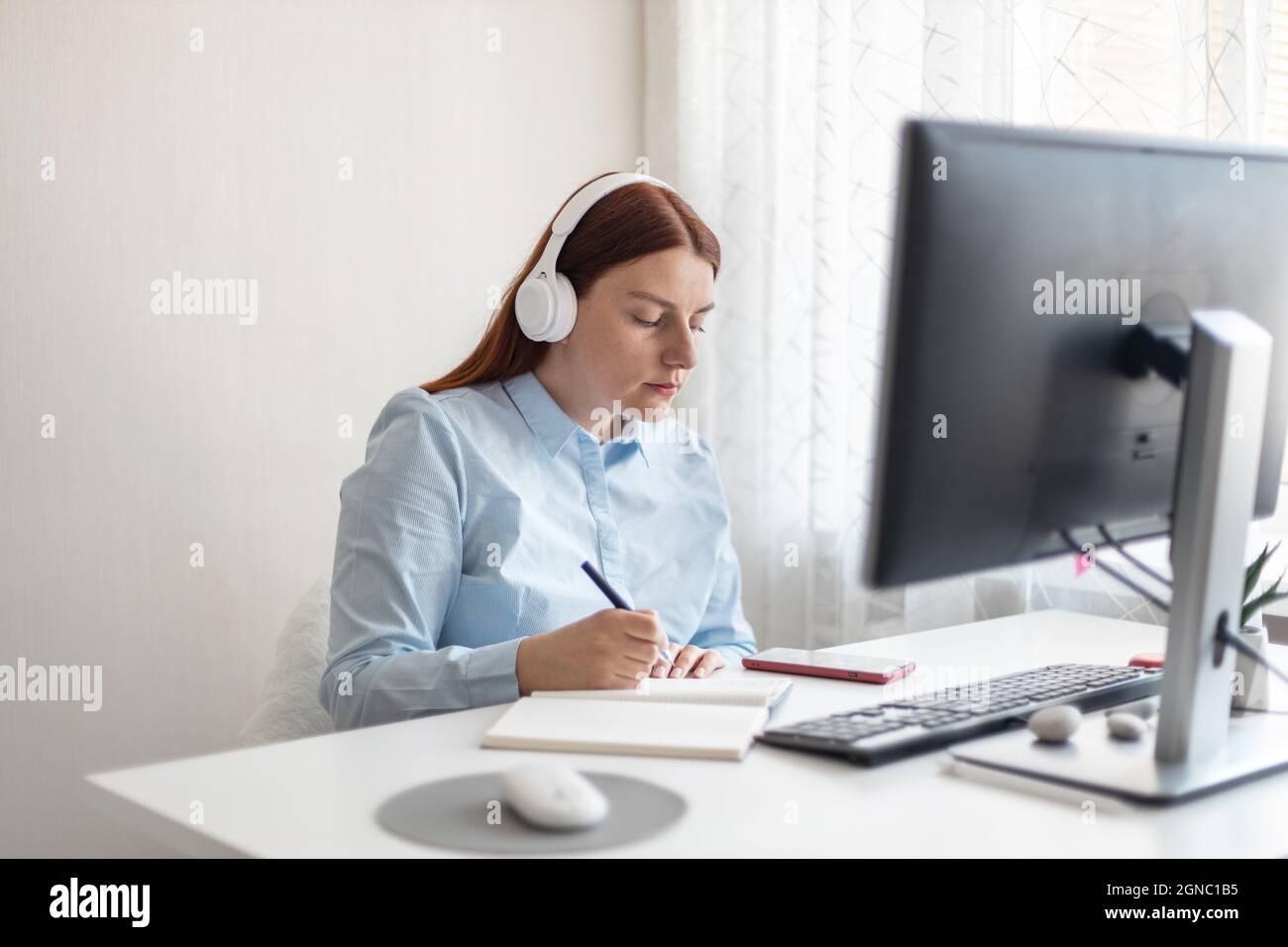 Apprentissage à distance, éducation et travail. Femme tenant le stylo à la main sur le bloc-notes à la maison, écrit des objectifs, des plans, faire à faire et liste de souhaits sur le bureau, à partir de Banque D'Images