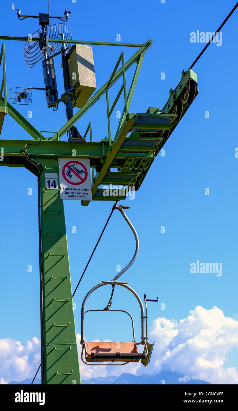 Pylône d'un télésiège avec planche « ne pas rebondir ou balancer les chaises » et une chaise avant le ciel bleu Banque D'Images