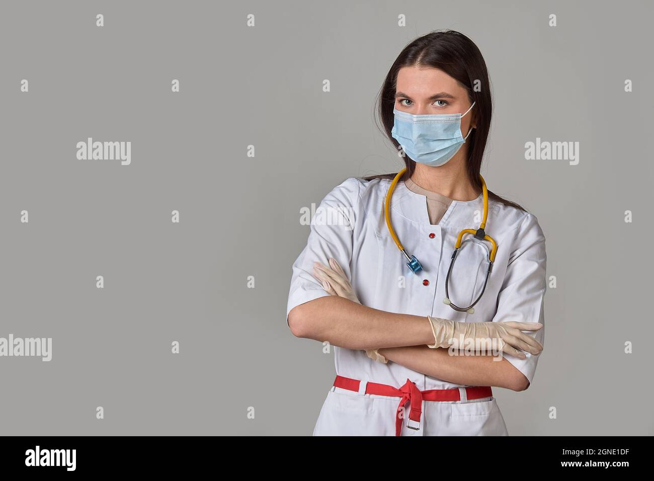 Une jeune femme médecin en manteau blanc avec un stéthoscope et un masque médical sur fond gris isolé Banque D'Images