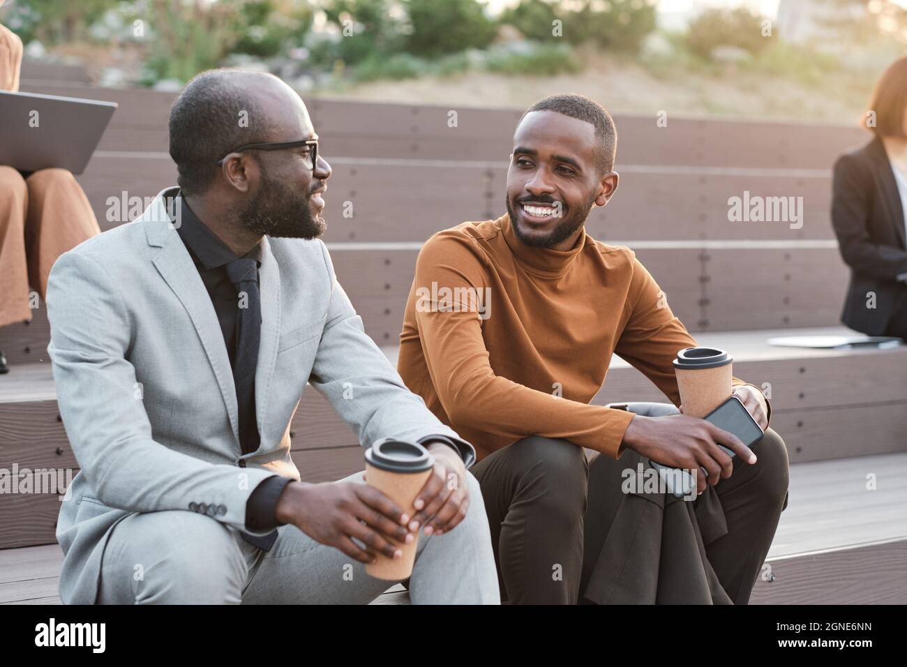 Plan horizontal moyen de deux hommes afro-américains élégants portant des tenues élégantes passer le temps de pause-café se détendre en plein air bavardant un Banque D'Images