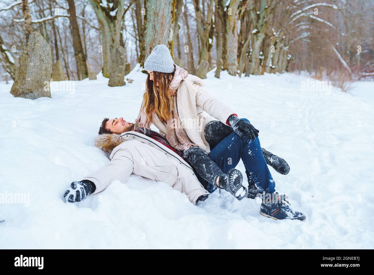 Un jeune couple heureux se trouve dans la neige, jette de la neige et joue  dans le parc d'hiver. L'homme et la femme s'amusent ensemble pendant les  vacances d'hiver Photo Stock -