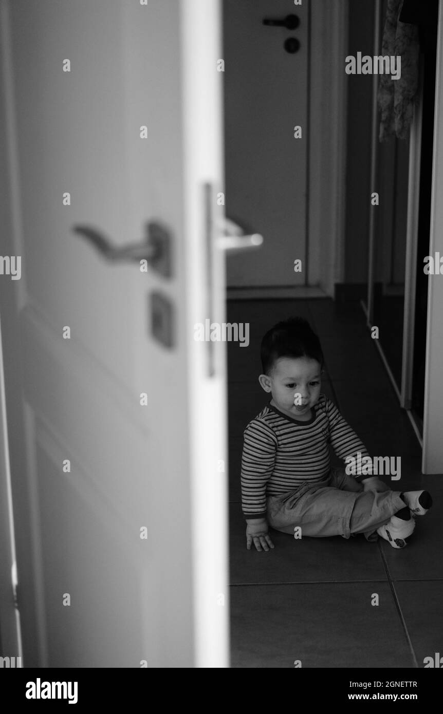 Photo en niveaux de gris d'un enfant mignon assis sur le sol Banque D'Images