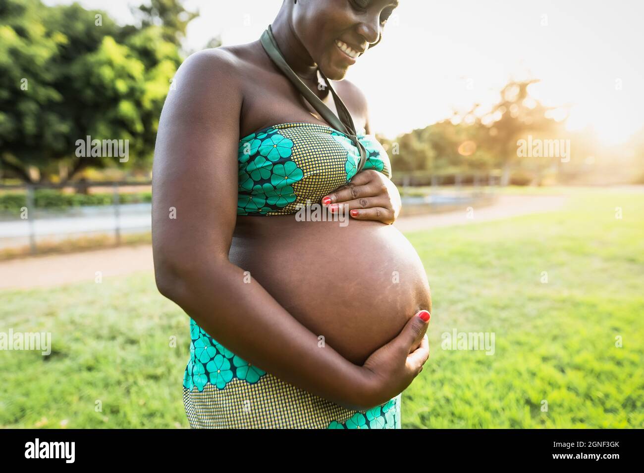 Gros plan ventre enceinte de la jeune femme africaine dans le parc pendant le coucher du soleil - concept de mode de vie de maternité Banque D'Images