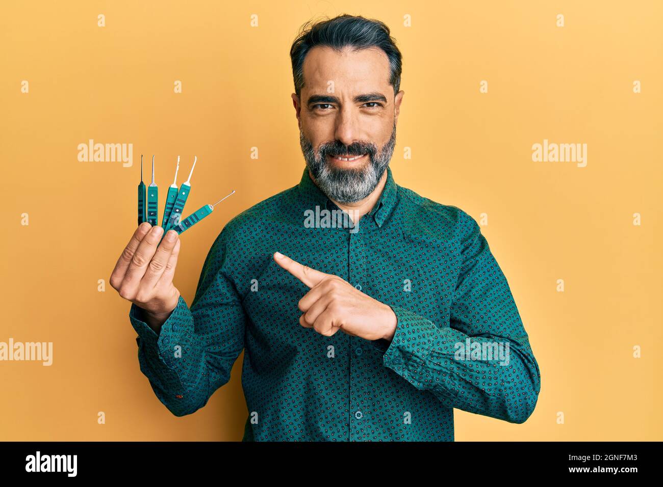 Homme d'âge moyen avec la barbe et les cheveux gris tenant le verrou de sécurité pour déverrouiller la porte de sécurité sourire heureux de pointer avec la main et le doigt Banque D'Images