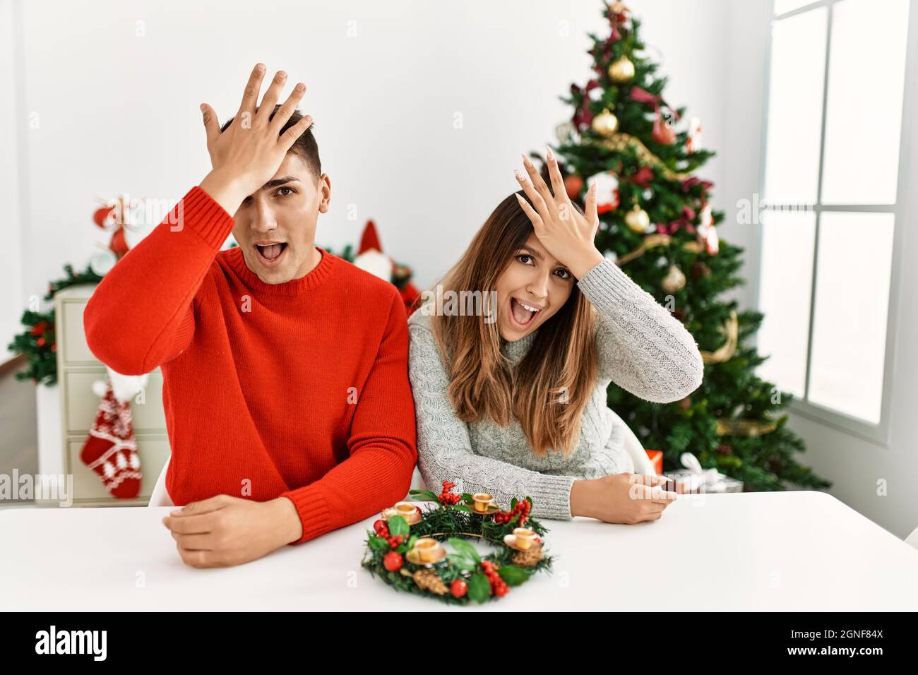 Jeune couple hispanique assis à la table à noël surpris avec la main sur la tête pour l'erreur, se souvenir de l'erreur. oublié, mauvais concept de mémoire. Banque D'Images Jeune couple hispanique assis à la table à noël surpris avec la main sur la tête pour l'erreur, se souvenir de l'erreur. oublié, mauvais concept de mémoire. Banque D'Images