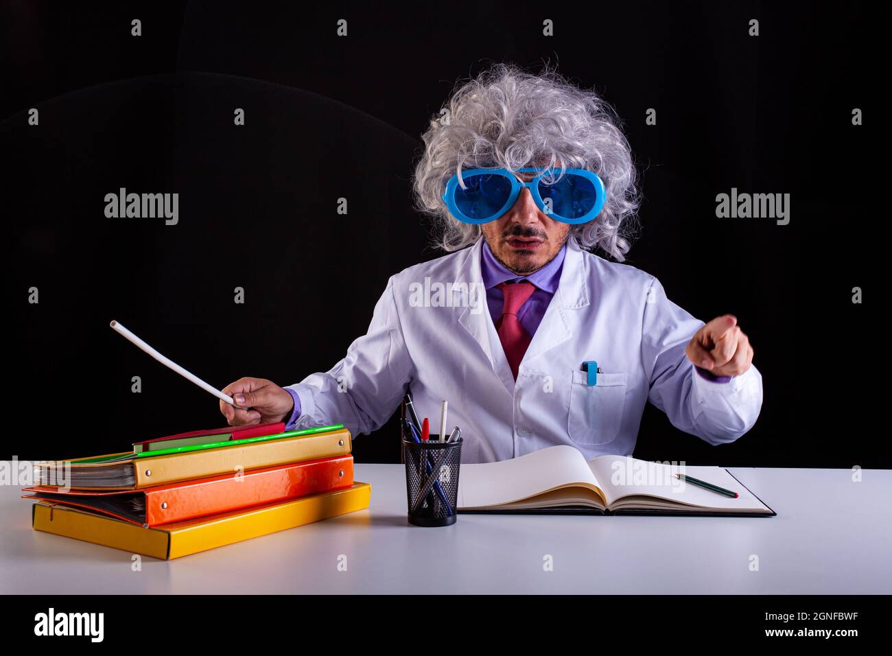 Professeur de science fou en manteau blanc avec des cheveux unkempt dans des lunettes drôles assis au bureau Banque D'Images