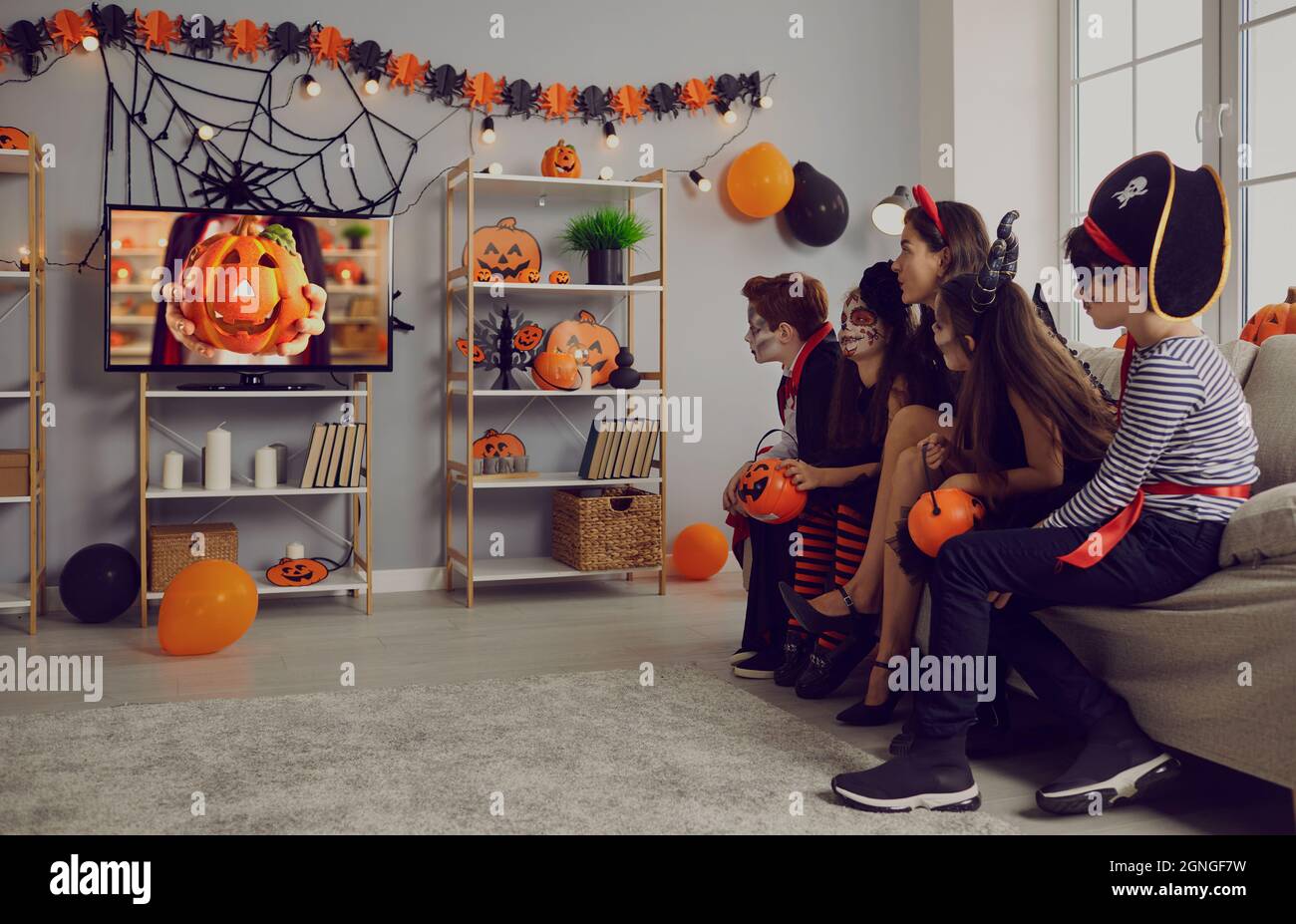 Enfants en costumes effrayants assis sur un canapé et regardant un film à la fête d'Halloween à la maison Banque D'Images