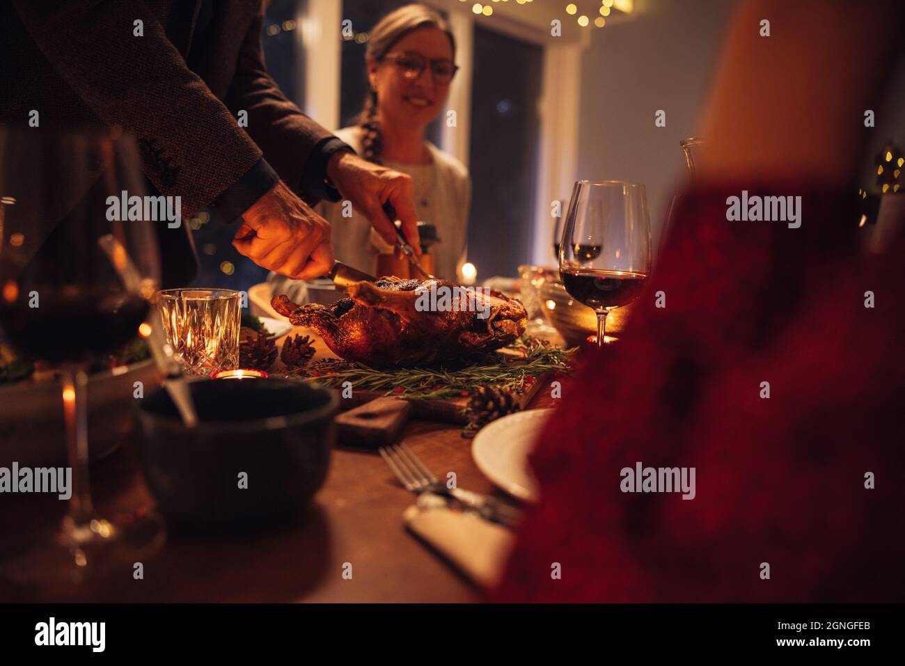 Homme senior servant de la dinde farcie traditionnelle torréfiée à la famille assise à table pour le dîner. La famille a dîné à la maison. Banque D'Images
