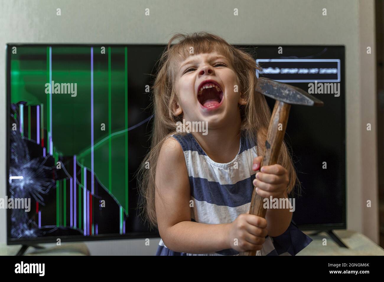 une fille a frappé la télé avec un marteau et rie de manière délirante. un enfant indiscipliné hyperactif Banque D'Images