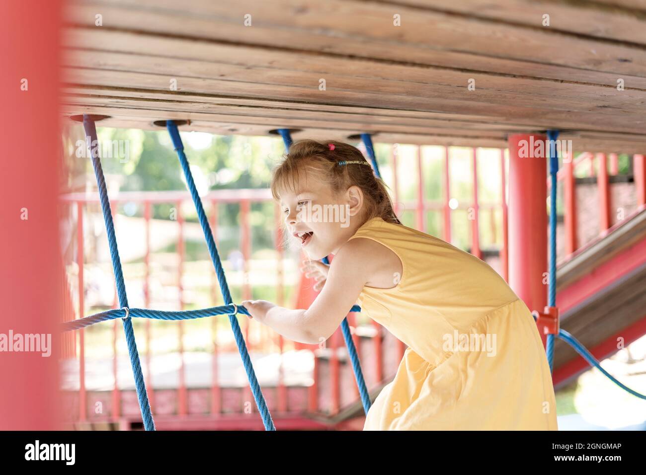 Les enfants jouent et grimpent à l'extérieur lors d'une belle journée d'été. Jolie fille dans une robe jaune sur une toile d'araignée Banque D'Images