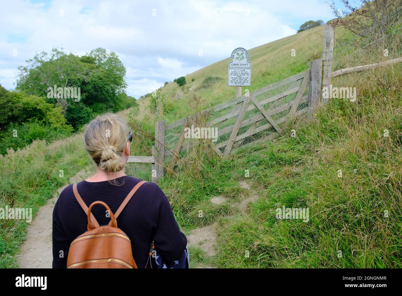 Femme caucasienne devant un panneau de confiance nationale pour Cerne Abbas craie figure géante à Dorset Banque D'Images