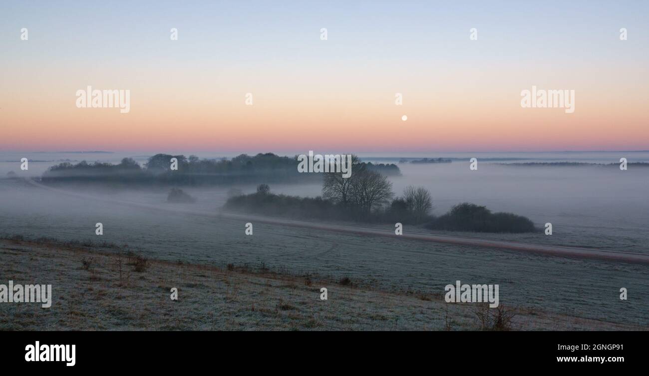 une brume matinale empli la vallée avec la lune de neige basse dans le ciel du lever du soleil Banque D'Images