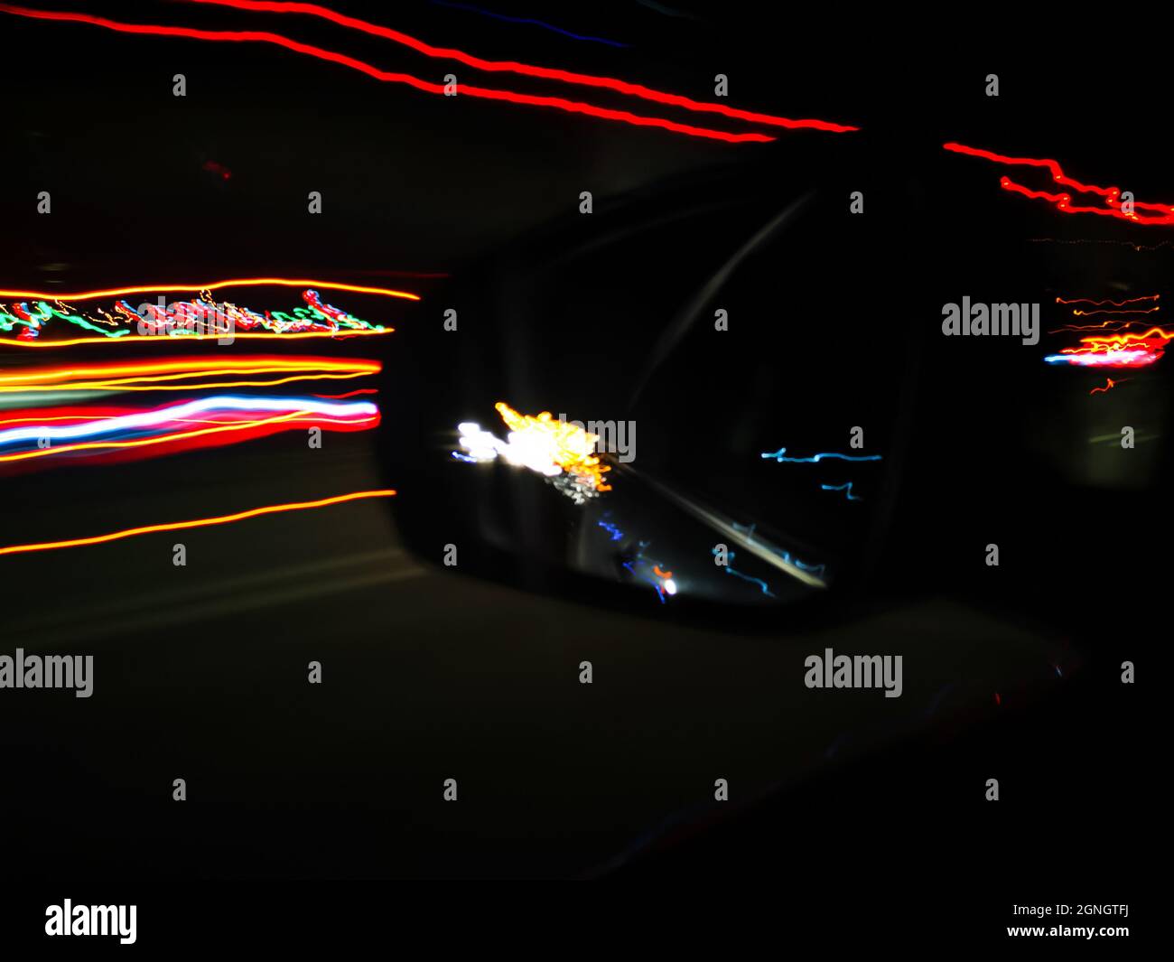 Les voies lumineuses bleues, orange et rouges au néon filent sur une longue exposition de la voiture à grande vitesse dans la ville nocturne et son reflet dans le rétroviseur Banque D'Images